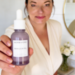 Close-up skincare shot of a woman holding a purple Herbivore Bakuchiol bottle forward with the label facing the camera.