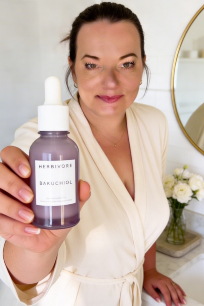 Close-up skincare shot of a woman holding a purple Herbivore Bakuchiol bottle forward with the label facing the camera.