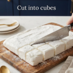 Sugar-free marshmallow slab being sliced into cubes on a wooden cutting board.
