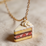 Mini strawberry layer cake slice pendant made from polymer clay on a gold chain.