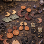 Handmade clay earrings with moon, celestial, and botanical details displayed on a dark surface with cutters, lavender, and witchy styling.