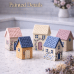 Mini handmade clay houses with pastel roofs, floral details, and textured surfaces displayed on a white quartz countertop in a bright kitchen.