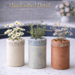 Three handmade clay flower frogs and herb holders filled with daisies, herbs, and soft flowers on a white quartz countertop in a blue kitchen.