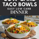Easy keto taco bowls with beef, lettuce, shredded cheese, avocado, salsa, and sour cream in a white bowl on a marble-style countertop with dark blue kitchen cabinets in the background.