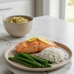 Plate of baked salmon topped with lemon slices, served with green beans and white rice on a light countertop.