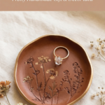Terracotta clay jewelry dish with pressed botanical details and a gold ring, styled on soft neutral fabric.