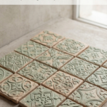 Textured handmade clay wall tiles in soft sage green and natural clay tones arranged in a decorative grid near a window.