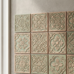Textured handmade clay wall tiles in soft sage green and natural clay tones arranged in a decorative grid near a window.