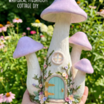 Handmade clay fairy house shaped like pastel purple mushrooms with a blue door, held outdoors in a flower garden.