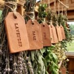 Bundles of dried herbs including lavender, sage, mint, chamomile, and rosemary hanging with handmade clay herb label tags in a wooden drying rack.