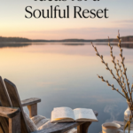 Wooden chair with a cozy blanket, open journal, and tea beside a calm lake at sunrise with spring branches in view.