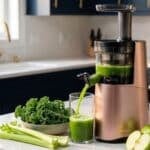 Hurom cold pressed juicer sitting on a white quartz counter with dark blue cupboards with gold hardware in the background. A mix of fruit sits on the counter beside it.