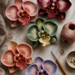 Flat lay of five large crocheted orchid flowers in gradient yarn colors including burgundy blush sage green peach and lavender on white marble with gold scissors and a wooden crochet hook