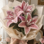 Pink crocheted stargazer-style lily flowers with delicate stamens loosely wrapped in brown kraft paper and tissue paper as a gift bouquet in warm soft lighting