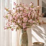Flat lay of crocheted carnations in red, pink, coral, and purple yarn scattered across cream linen with a bouquet wrapped in kraft paper and tied with twine