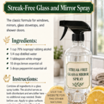 Clear glass trigger spray bottle labeled Streak-Free Glass and Mirror Spray beside sliced lemons and fresh mint leaves on a white marble surface with a bright bathroom window in the background. Essential oil cleaning spray recipe by Aligned Design.