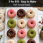 Overhead product display of twelve polymer clay donut fridge magnets in assorted glaze colors arranged on a white surface with a handwritten price tag reading 3 for dollar 15