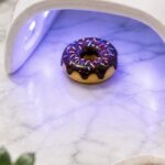 Purple UV light curing a finished polymer clay donut magnet in chocolate and ivory glaze colors on a light surface with crafting tools visible nearby