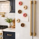 Cluster of handmade polymer clay donut fridge magnets in assorted glaze colors displayed on a white and gold kitchen refrigerator door in a styled home kitchen