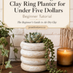 Pinterest pin graphic showing a white distressed textured air dry clay stacked ring planter holding a blue-green echeveria succulent and trailing string of pearls plant, styled on a wooden shelf with books, a lit amber candle, and trailing ivy, with cream text overlay for a beginner's clay idea guide on jenniferdawn.ca.