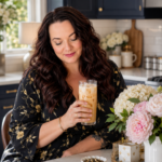 Plus-size woman with dark mahogany hair in a luxury modern farmhouse kitchen with dark navy cabinetry and brushed gold hardware holding an iced jasmine tea drink, 10 low carb jasmine tea recipes