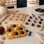Flat lay of three food-themed clay tic tac toe boards on a white quartz countertop, including a waffle board with butter and blueberry pieces, a donut vs. cookie board, and a berry-themed board, styled in a luxury navy and gold kitchen.