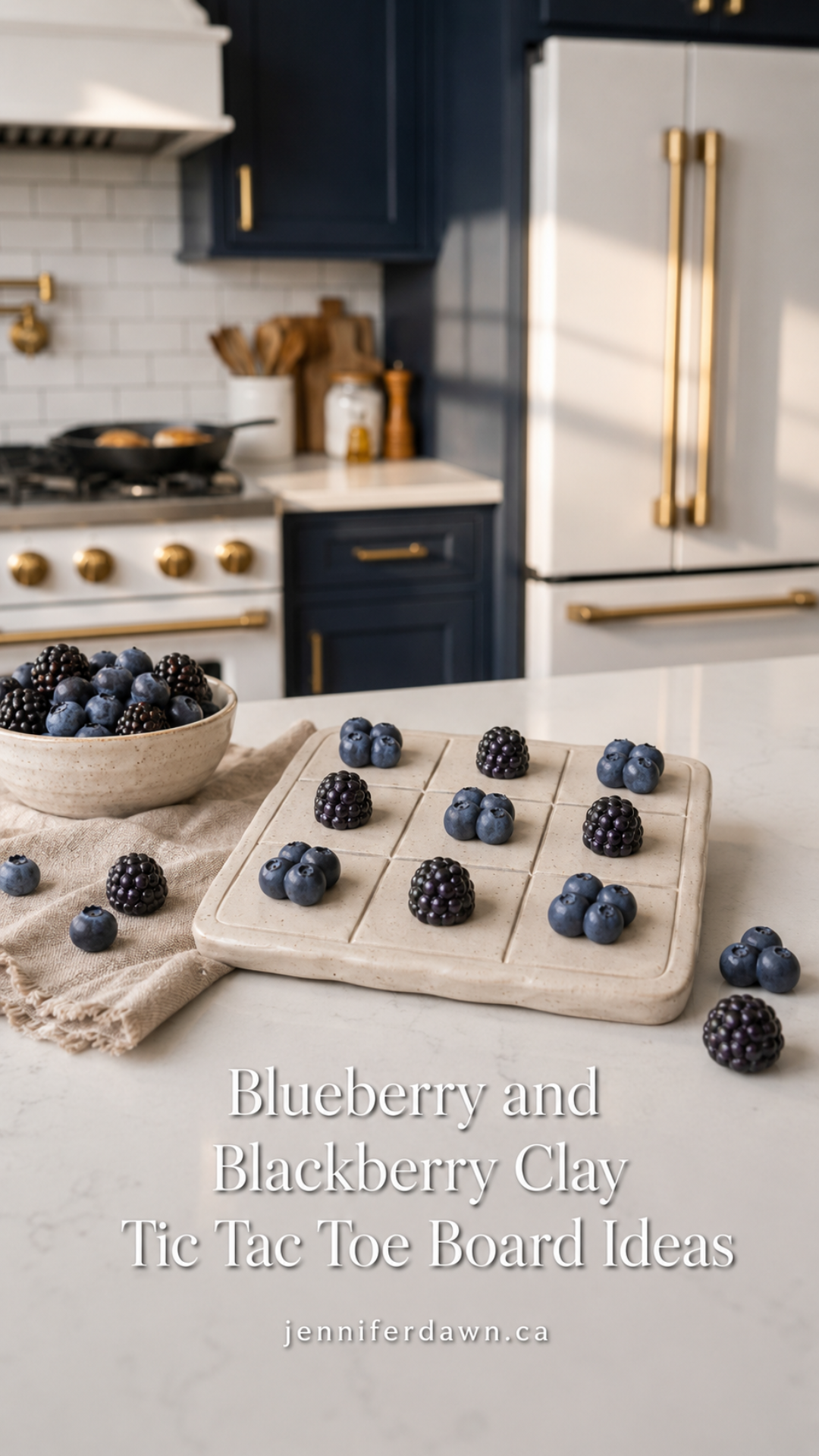 Cream textured clay tic tac toe board with blueberry cluster and blackberry playing pieces on a white quartz countertop, styled with a bowl of fresh berries and a linen napkin, navy cabinetry and gold refrigerator visible in the background.