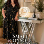 Close-up of a mirrored glass console table with sparkling crystal accent legs, topped with a round light fixture, books, a diffuser, and a textured white vase against a neutral wall.