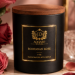 Bohemian Rose handcrafted soy candle by Aligned Design in a matte black vessel with gold foil crest label and wooden lid, surrounded by deep pink roses and scattered rose petals on a marble surface.