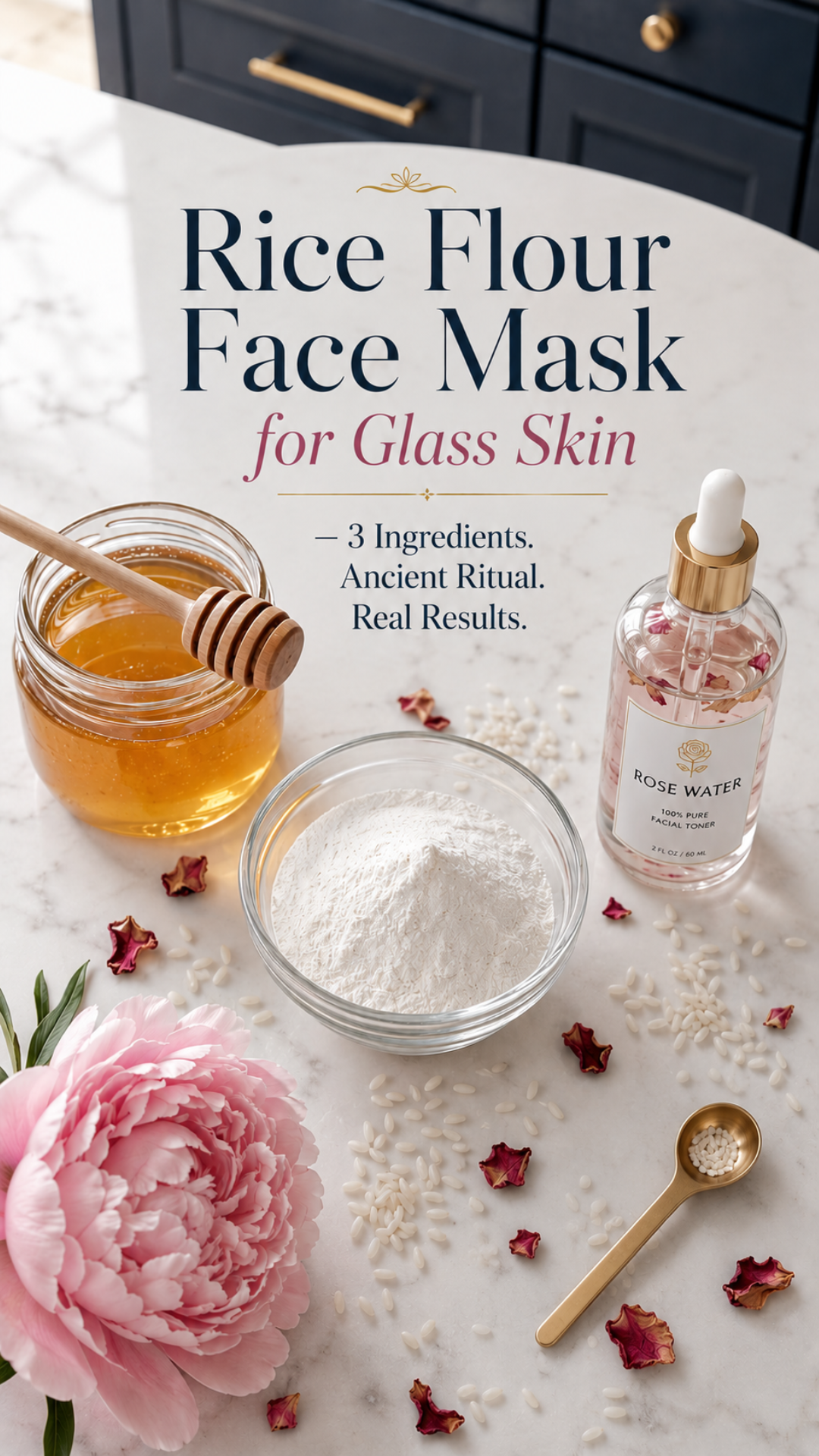 Overhead flat lay of rice flour face mask ingredients on white marble countertop with dark navy cabinetry — glass bowl of rice flour, honey jar with wooden dipper, rose water bottle, pink peonies, scattered rose petals, and gold measuring spoon.