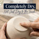 Close-up of hands holding an upturned unsealed air-dry clay bowl on a warm oak surface, one finger pressing gently against the base to check dryness, styled with dried florals and a lit candle in the background, titled "The One Rule Before You Seal: Completely Dry, Not Just Dry to the Touch"