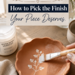 A terracotta air-dry clay scalloped trinket dish with a botanical leaf imprint being brushed with water-based satin varnish on a warm oak surface, showing the difference between the raw matte side and the freshly sealed glossy side, beside an open jar of Water-Based Varnish Satin Finish and dried florals, titled "Matte, Satin, or Gloss? How to Pick the Finish Your Piece Deserves"