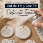 Hand spraying clear acrylic matte sealer over a collection of unsealed air-dry clay ornaments with delicate botanical leaf imprints in circular, heart, and hexagon shapes arranged on kraft paper beside dried florals, titled "The Fastest Method — and the Only One for Delicate Texture"