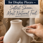 Hands buffing clear matte finishing wax onto a handmade white air-dry clay curved sculptural vase with an organic circular cutout, styled on a warm oak surface beside an open tin labeled Clear Finishing Wax Matte Natural Non-Toxic, dried pampas grass in a ribbed vessel, and a linen napkin, titled "The Stone-Look Finish for Display Pieces — Softest Sheen, Most Natural Feel"