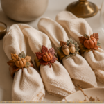 Four air-dry clay napkin rings decorated with sculpted leaves, mini pumpkins, and acorns in warm autumn tones, wrapped around folded cream linen napkins on a fall tablescape with a brass candle holder