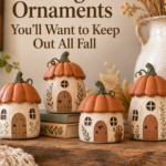 Four small handmade clay cottage ornaments with tiny pumpkin-shaped roofs painted in warm cinnamon and cream, each with a hand-carved arched door and window, arranged on a wooden mantel with a soft knit throw hanging nearby.