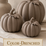 Three color-drenched air dry clay pumpkins in warm mushroom taupe with matching body, stem, and leaves on a cream linen runner