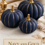 Three matte navy and gold air dry clay pumpkins with hand-painted gold vertical lines on a white quartz surface with dried hydrangea