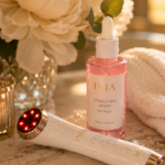 Luxury Pinterest pin featuring an at-home red light therapy skincare device and conductive serum displayed on a marble vanity with white flowers, spa towels, and warm golden lighting. The image highlights an LED facial device used alongside Korean skincare to support glowing, hydrated, youthful-looking skin and elevate an anti-aging skincare routine.