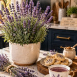 Blooming lavender plant with tall purple flower spikes in a cream ceramic pot on a white quartz countertop, dark navy cabinetry blurred behind, small plate of lavender shortbread cookies and a delicate porcelain teacup of lavender tea in the foreground, dried lavender sprigs tied with twine, brushed gold spoon and honey pot nearby, warm natural light.