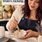 A woman with dark red hair in a cream sweater and navy apron brushing sealer onto a scalloped air dry clay trinket dish at a marble kitchen counter, with a jar of sealer, lavender, white hydrangeas, and candles nearby. The text reads "The Step That Stops Clay Gifts from Cracking."