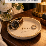 A cream air dry clay trinket dish with a gold rim, stamped with the initials J and C, a heart, and a date, holding a men's watch and a ring on a wooden nightstand. The text reads "Couples Initials Clay Dish, A Sweet Handmade Gift for Him" and "Tap for the Full List." Board: Handmade Gifts for Him