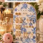 An arched air dry clay earring stand covered in a blue and white floral pattern with a gold edge, holding rows of gold hoops, studs, and pearl drop earrings on a mirrored vanity tray with a pink ranunculus and perfume. The text reads "DIY Clay Earring Stand, Made in 10 Minutes, Loved All Year" and "Save This Gift Idea."