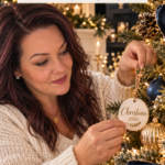 A woman in a cream sweater hanging a round air dry clay ornament, personalized with a name and 2026, on a navy and gold Christmas tree. The text reads "Personalized Clay Ornaments, The Gift They'll Hang Every Year" and "Save for Christmas." Board: Air Dry Clay Christmas Ornaments