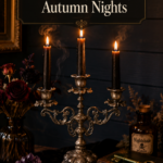An ornate antique-silver three-arm candelabra with intricate baroque scrollwork holds three tall black tapered candles softly lit on a weathered dark wood side table draped with black velvet, styled with dried black roses and burgundy ranunculus in a smoky glass vase, a raw amethyst crystal cluster, polished obsidian, an antique brass skeleton key, worn leather spellbooks, and a dark amber apothecary bottle for a moody witchy fall vignette.