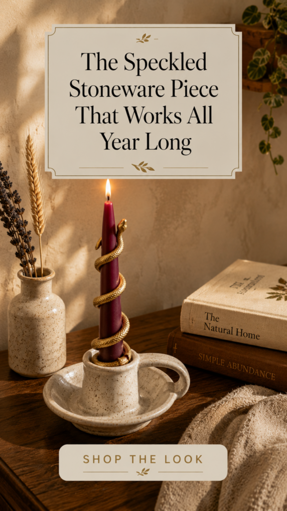 rustic speckled cream stoneware chamberstick tealight holder with a small curved side handle and matte speckled glaze holds a lit ivory pillar candle on a warm oak side table, styled with a matching speckled bud vase holding dried wheat and lavender, vintage hardcover books, and a folded chunky oatmeal linen throw for an effortless cozy wabi-sabi fall vignette.