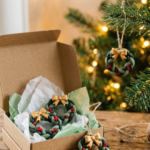 Small braided green polymer clay wreath ornaments with red berries and gold bows, in a kraft gift box and hanging on a Christmas tree.