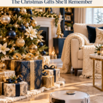 A white robot vacuum cleans a sunlit oak floor beside a Christmas tree decorated in navy and gold, with wrapped gifts underneath, a cream armchair with a chunky knit throw, and a decorated fireplace in the background.