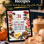 A tablet showing the cover of a 31 low carb no-bake dessert recipes ebook with keto cheesecake jars, berry parfaits, lemon bars and chocolate truffles, propped on a white quartz kitchen counter beside a plate of sugar-free pumpkin spice marshmallows, a pumpkin spice latte, cinnamon sticks, an orange pumpkin and cream flowers in front of navy kitchen cabinets.